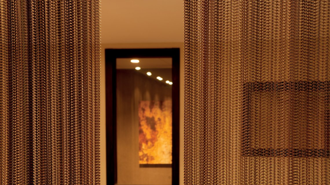 Cortinas em malha metálica MIES efeito enferrujado – Arquitetura de interiores hotel Paris - <p>Instalação de cortinas em malha metálica espiralada MIES com acabamento efeito enferrujado estabilizado no âmbito da renovação do Hôtel Villa de Saxe, em Paris. A malha metálica sob medida acrescenta profundidade, textura e filtragem luminosa a um projeto de arquitetura de interiores de alto padrão.</p>