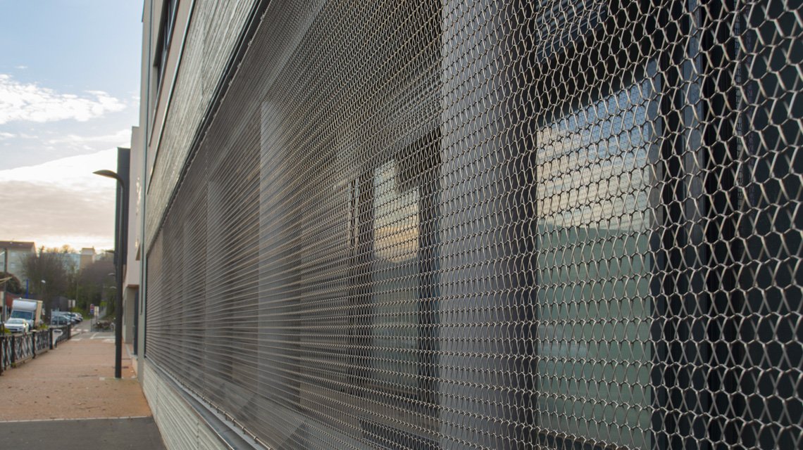 Malha metálica brise-soleil diante das superfícies envidraçadas - <p>Vista aproximada da malha metálica TORROJA F instalada diante das superfícies envidraçadas do Collège Françoise Héritier, em Noisy-le-Sec. A malha espiral em aço inoxidável forma uma trama metálica aberta utilizada como brise-soleil.</p>