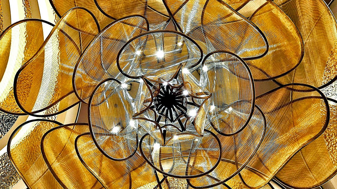 Restaurante Le Voyage – Iluminação em malha metálica arquitetónica - <p>Vista do lustre em malha metálica arquitetónica integrado na arquitetura de interiores do restaurante Le Voyage, a bordo do Celebrity Xcel. Um projeto que alia design, luz e inovação.</p>