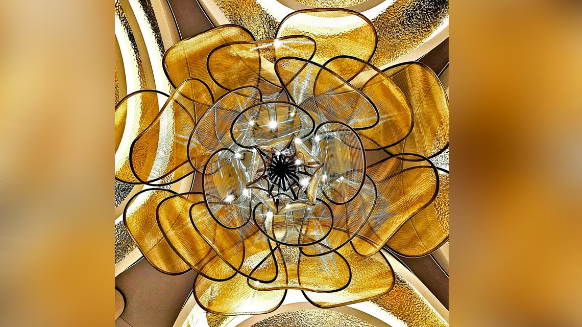 Vista inferior do lustre em malha metálica - <p>Vista central do lustre monumental em malha metálica arquitetónica, evidenciando a sua estrutura circular e os efeitos de luz criados pela transparência da malha.</p>