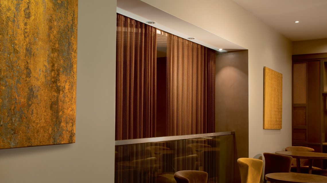 Malha metálica arquitetónica MIES – Resilha interior efeito enferrujado - <p>Malha metálica espiralada MIES utilizada como revestimento mural e elemento decorativo num projeto hoteleiro em Paris. O acabamento efeito enferrujado estabilizado reforça a identidade contemporânea e acolhedora do espaço.</p>